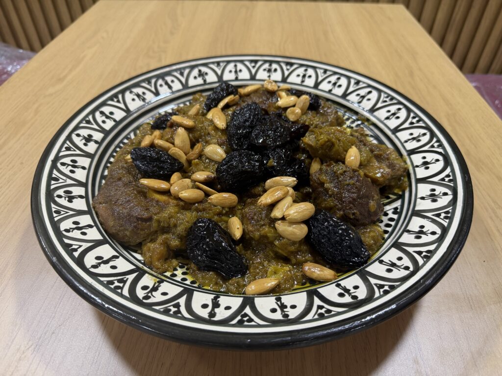 طبق اللحم بالبرقوق واللوز في صحن مغربي مزخرف من شهيوات أم قصي بطنجة