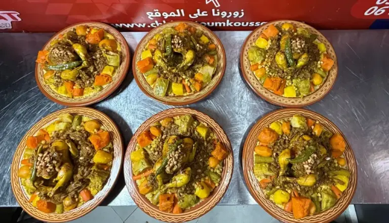 ستة أطباق من الكسكس المغربي بالدجاج والخضر مرتبة في مطبخ شهيوات أم قصي بطنجة